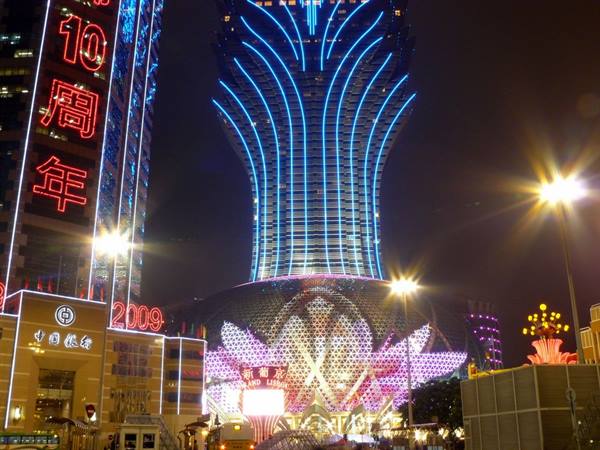 Grand Lisboa casino glowing blue and pink at night among Chinese neon signs