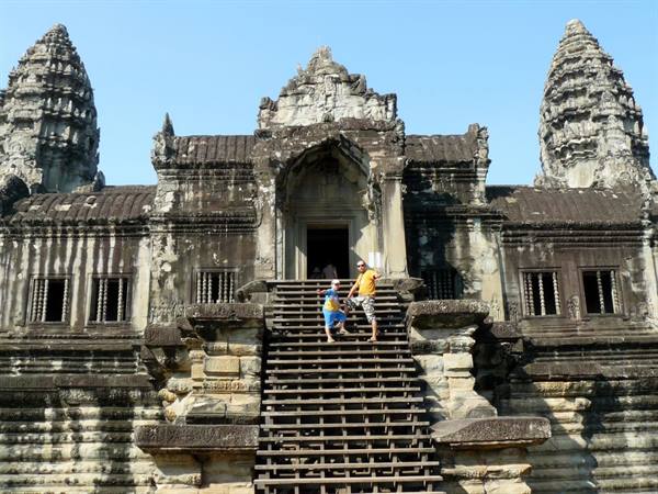 Tourists descend the stone staircase of Angkor Wat, ancient towers and blue sky