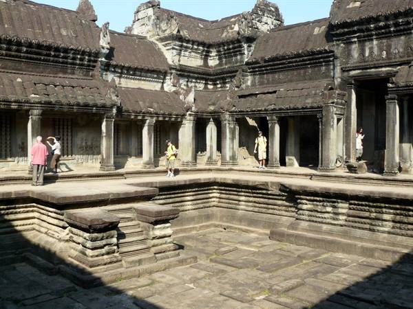 Tourists in the stone courtyard of Angkor Wat, covered galleries under sunlight