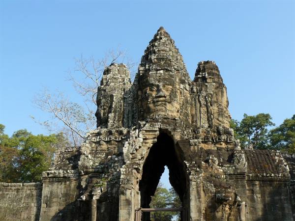 Stone gate with carved face at Angkor Thom under blue sky