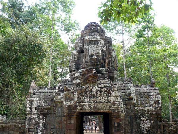 Stone gate with carved smiling faces at Angkor, tourists beneath the tower