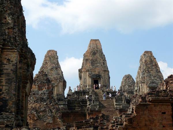 Tourists climb the stone staircase of Pre Rup temple under a blue sky
