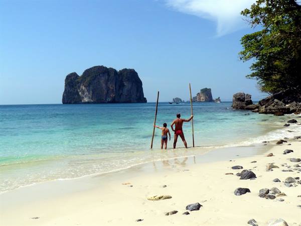 Father and son with long wooden poles in turquoise water by limestone karsts, Krabi