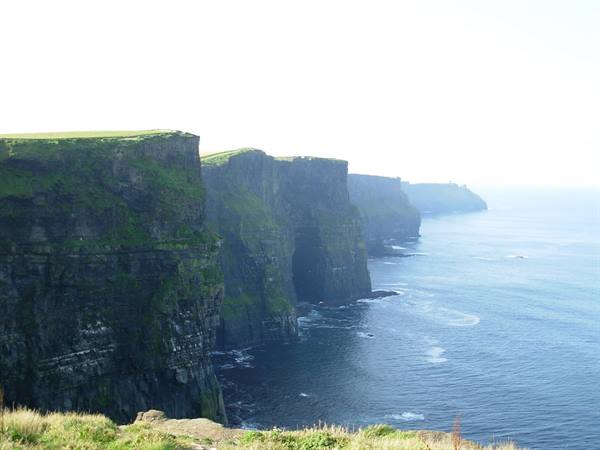 Cliffs of Moher: green rock walls above the ocean, clear light, waves on rocks