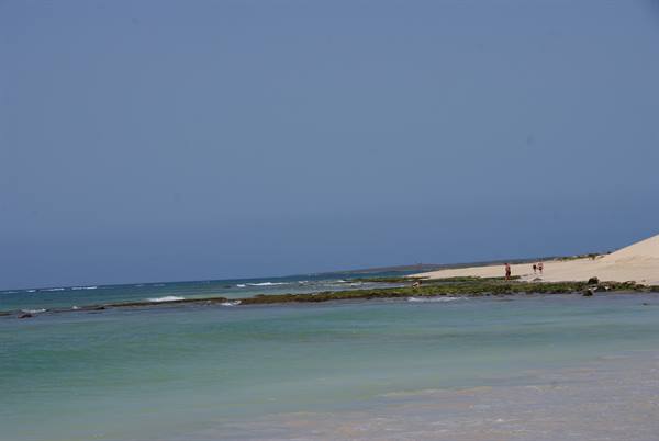 Pale sand beach with dune and people, turquoise water under a blue sky