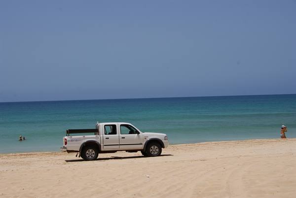White pickup truck on the sand in front of turquoise sea, swimmers in the water