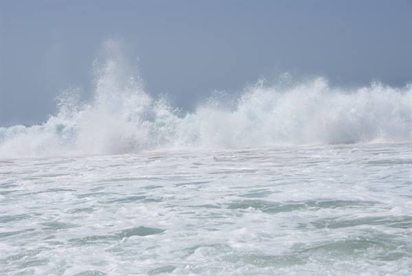Ocean waves crash into white foam under a blue sky