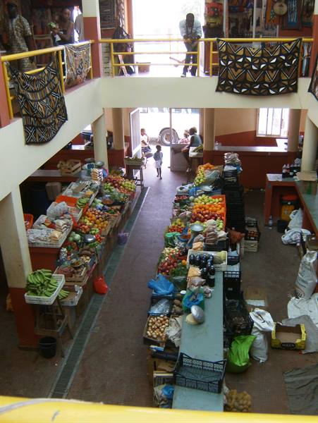 Two-story covered market with fruit stalls and patterned textiles on the railings