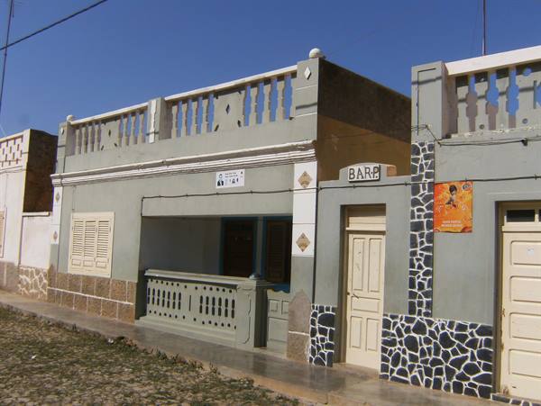 Grey colonial houses with balcony and bar sign on sandy street