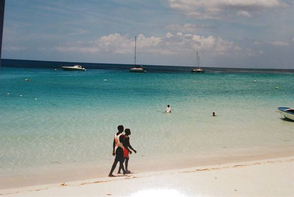 Two boys walk on white sand, sailboats on turquoise sea