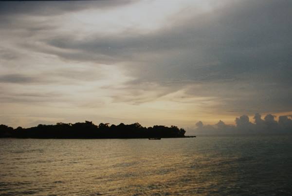 Dark tree-covered island seen from the sea, boats and golden light on water