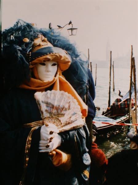 White carnival mask in Venice holding a fan beside the lagoon
