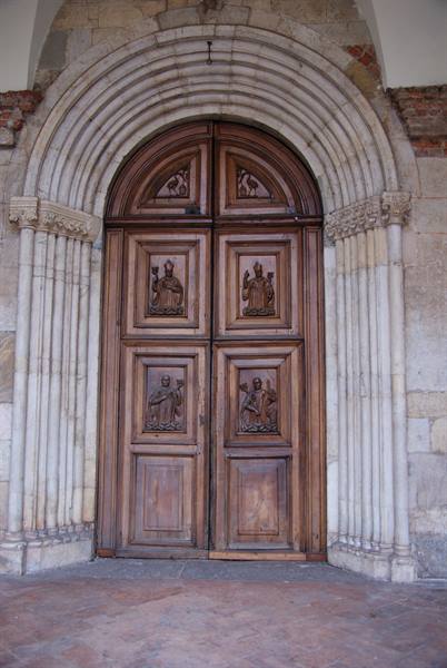 Carved wooden door with saints, framed by Romanesque stone arches