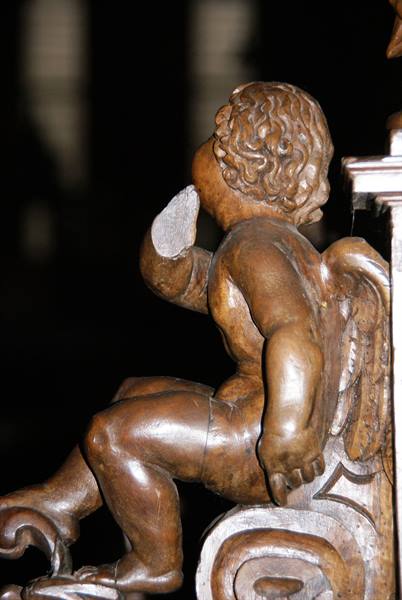 Carved wooden winged cherub with damaged arm, warm side lighting