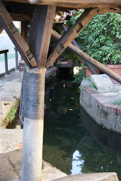 Wooden beams on stone pillar above a water channel with bricks and plants