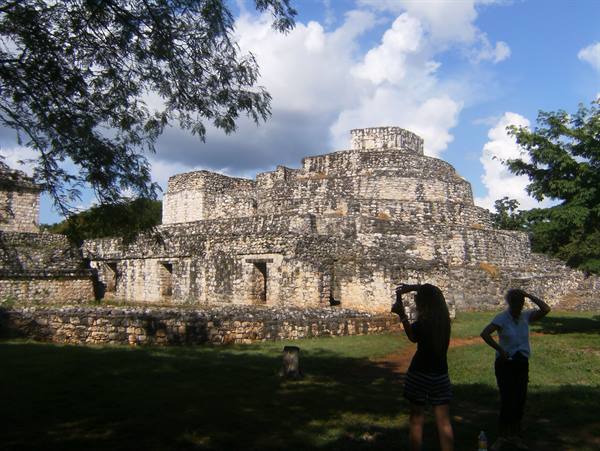 Tourist photographs the round stone pyramid of Ek Balam among trees