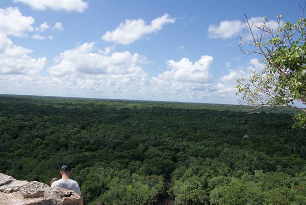 Tourist on Maya stone overlooking green jungle under white clouds, Coba