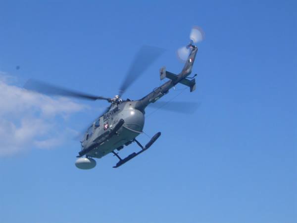 Grey military helicopter flying against blue sky with spinning rotor