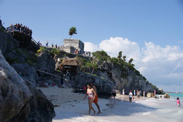 Tourists on the beach below the Mayan ruins of Tulum, rocks and palms