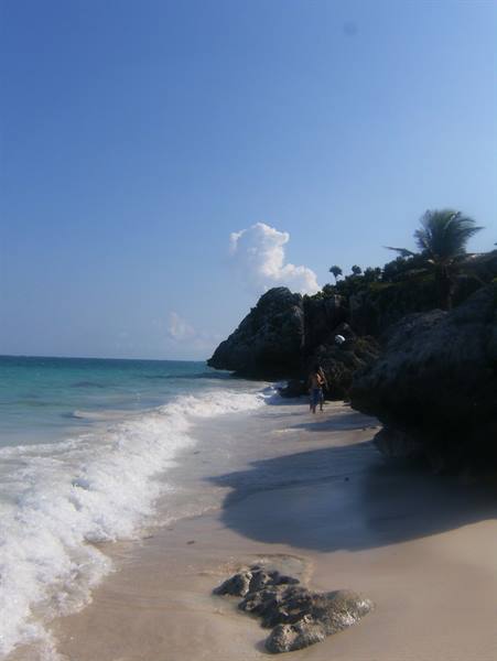 Tourist walking on sand beneath Tulum's rocks and palm trees