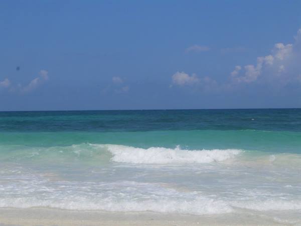 White wave breaking on pale sand, turquoise sea under blue sky