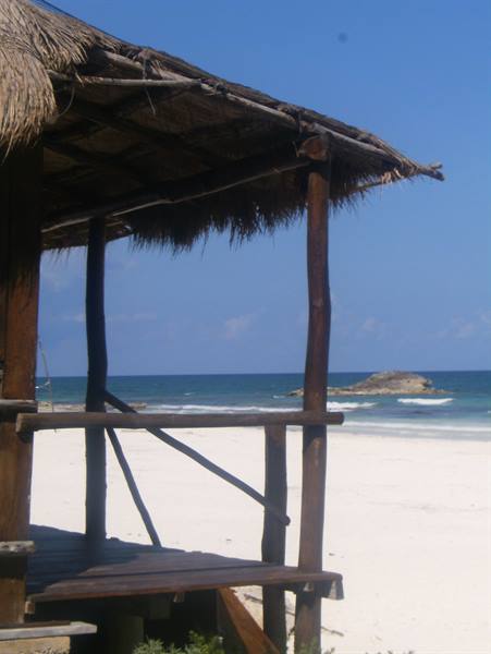 Wooden thatched palapa hut on white sand facing turquoise sea