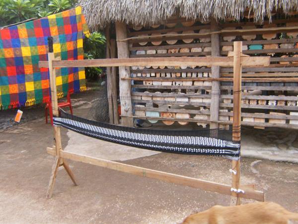 Wooden loom with black and white fabric, thatched hut and colorful textiles