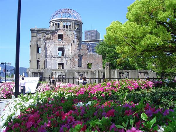Hiroshima's Genbaku Dome among pink flowers and tourists under sunny sky
