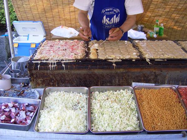 Cook in Asahi apron grilling takoyaki on iron griddle at street stall