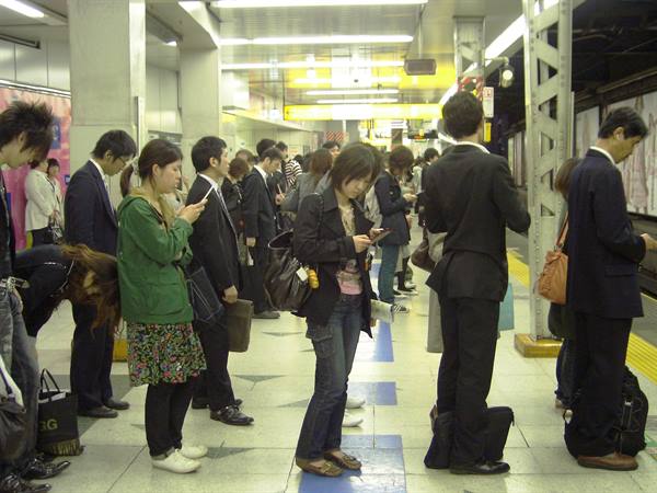 Commuters waiting on a Tokyo subway platform, many checking their phones
