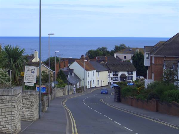 Road sloping down past thatched cottages, calm blue sea beyond the rooftops
