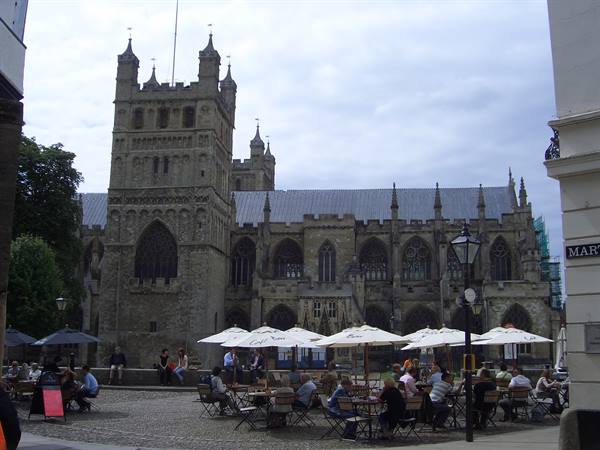Exeter Gothic stone cathedral, people seated at café tables under white umbrellas