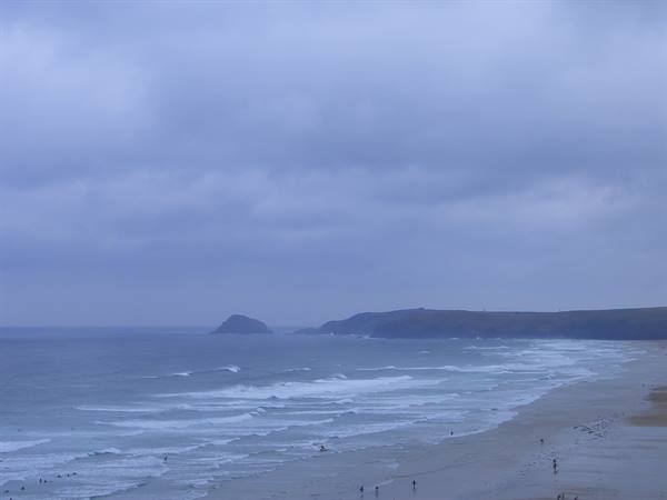 Beach under cloudy sky, ocean waves and swimmers on the sand