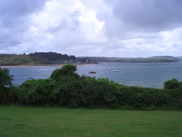 Boats in bay under cloudy sky, green bushes and lawn in foreground