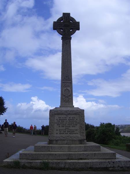 Granite Celtic cross war memorial with tourists walking beneath a cloudy sky