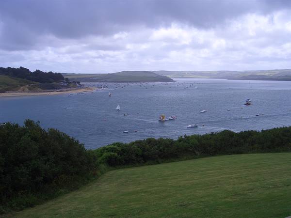 Boats and a sailboat on the estuary, sandy beach and green hills under cloudy sky