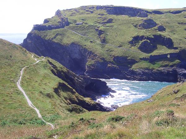 Footpath winds down grassy cliffs to rocky cove with turquoise waves