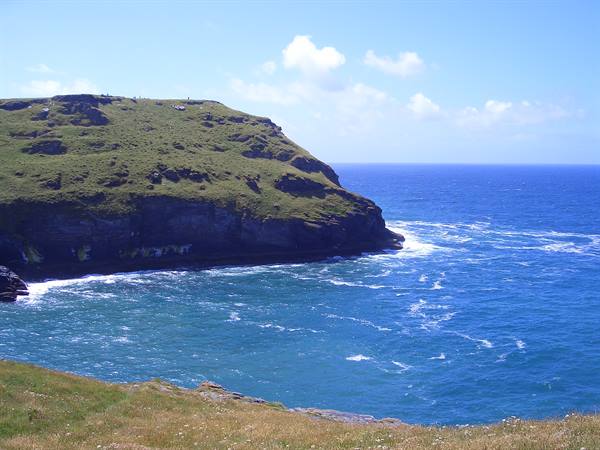 Grassy headland with steep cliffs over blue ocean, white waves on rocks