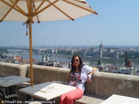 Woman sitting under a sun umbrella in Budapest, Parliament and Danube behind her