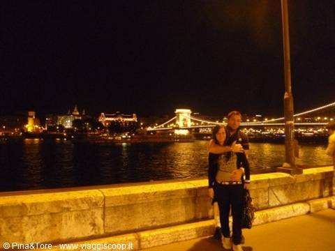 Couple embracing at night by the Danube, Chain Bridge lit up behind in Budapest