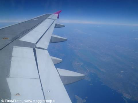 Airplane wing with pink winglet over blue islands and sea