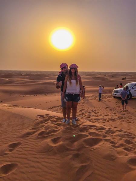 Couple in red headscarves on sand dune under low sun