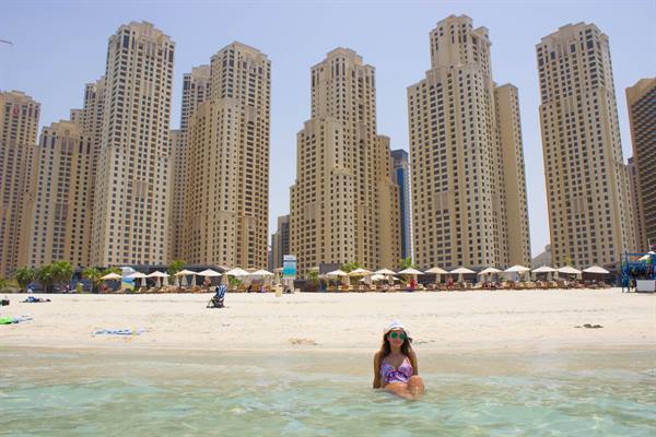 Woman sitting in turquoise water at JBR Beach, skyscrapers behind