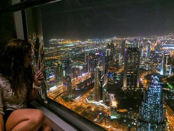 Girl at Burj Khalifa points at Dubai's illuminated skyscrapers at night