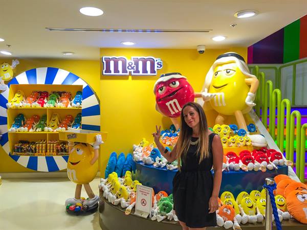 Woman posing next to giant M&M plush characters in a colorful store