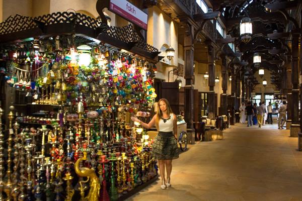 Woman beside a stall of colorful lanterns and shisha pipes in a wooden souk