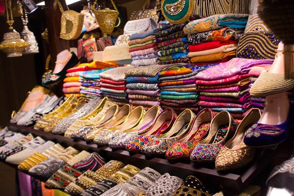 Market stall with colorful scarves and embroidered flat shoes under warm lights