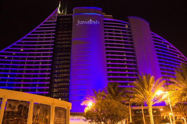 Jumeirah hotel lit up in purple at night, palms and streetlights below