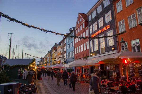 Nyhavn, Copenhagen: colorful lit townhouses, Christmas market stalls and people along the canal