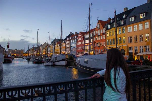 Girl on a bridge looking at colorful townhouses and boats of Nyhavn, Copenhagen